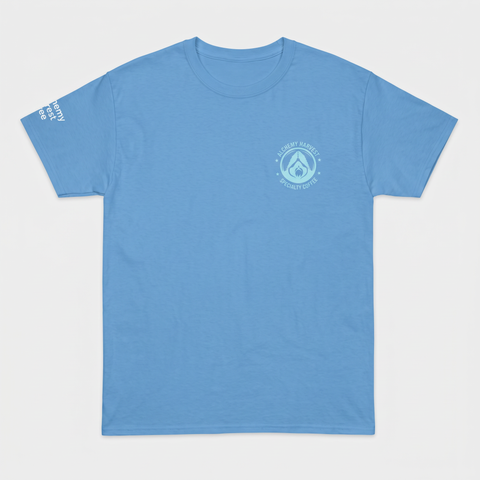A light blue crewneck t-shirt with a small circular logo on the left chest and white text on the right sleeve, displayed flat against a light gray background.