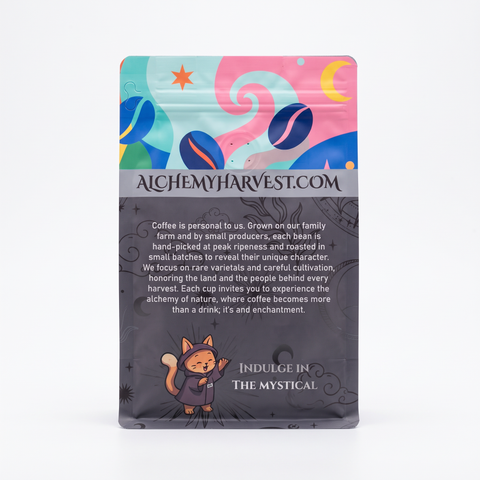 A stand-up pouch of Alchemy Harvest coffee on a clean white background. The packaging features a colorful abstract illustration at the top with blue, pink, and yellow shapes, a gray band with the website 'ALCHEMYHARVEST.