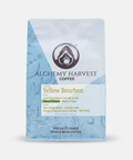 A stand-up coffee bag labeled Alchemy Harvest Coffee Yellow Bourbon, shown on a clean white background. The packaging is light blue with darker blue decorative line art and a central white label area with black and yellow text.