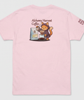 A light pink short-sleeve t-shirt shown flat against a light gray background. The back of the shirt features a cartoon graphic of an orange cat dressed as an alchemist pouring coffee, with the text 'Alchemy Harvest Coffee' above it.
