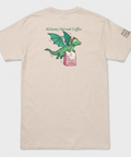 A light beige crewneck t-shirt shown from the back, featuring a cartoon green dragon holding a pink coffee bag with the text 'Alchemy Harvest Coffee' above it. The right sleeve has 'ALCHEMY.