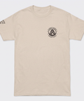 A light beige crewneck t-shirt with a black circular logo on the left chest reading 'ALCHEMY HARVEST COFFEE' and a small black text print on the right sleeve.
