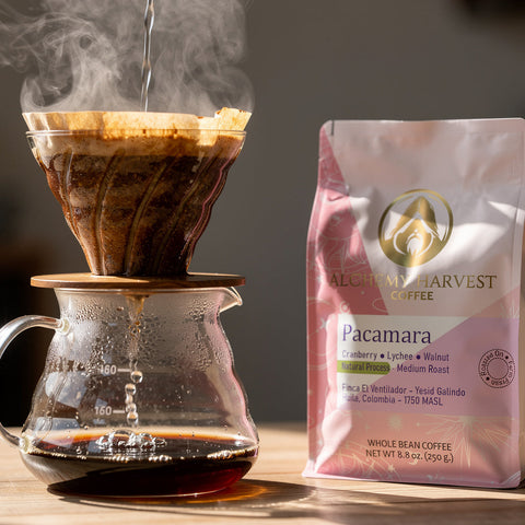 Drip coffee being brewed with a bag of Alchemy Harvest Pacamara coffee on a wooden surface.