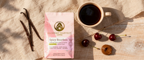 Alchemy Harvest Coffee package with a cup of coffee, vanilla beans, and cherries on a wooden surface.
