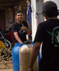 Marlon and his brother standing next to large containers where coffee currently ferments