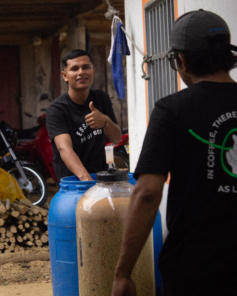 Marlon and his brother standing next to large containers where coffee currently ferments