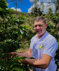 Nelson Urrego standing among coffee plants with a scenic background