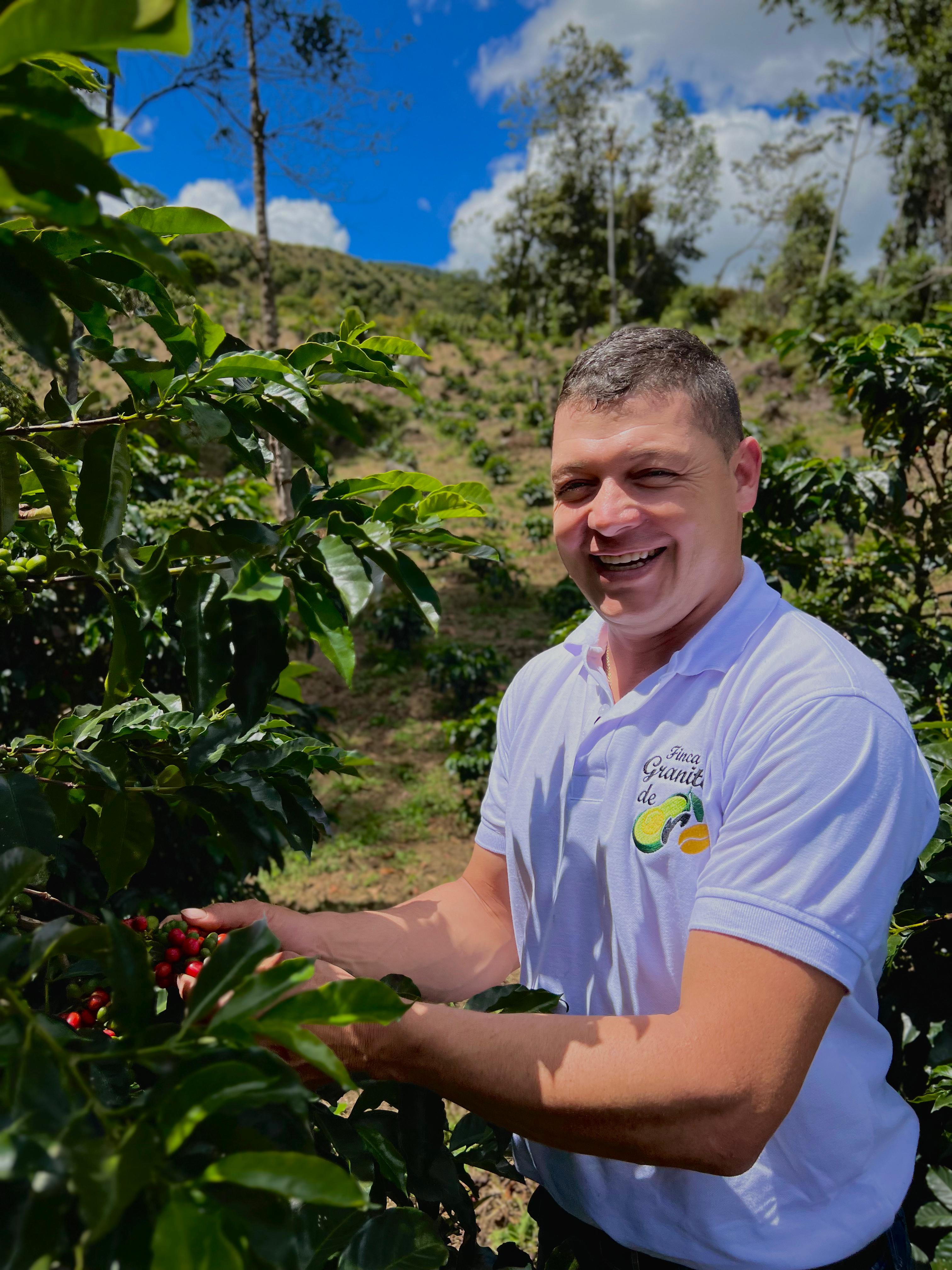Nelson Urrego standing among coffee plants with a scenic background